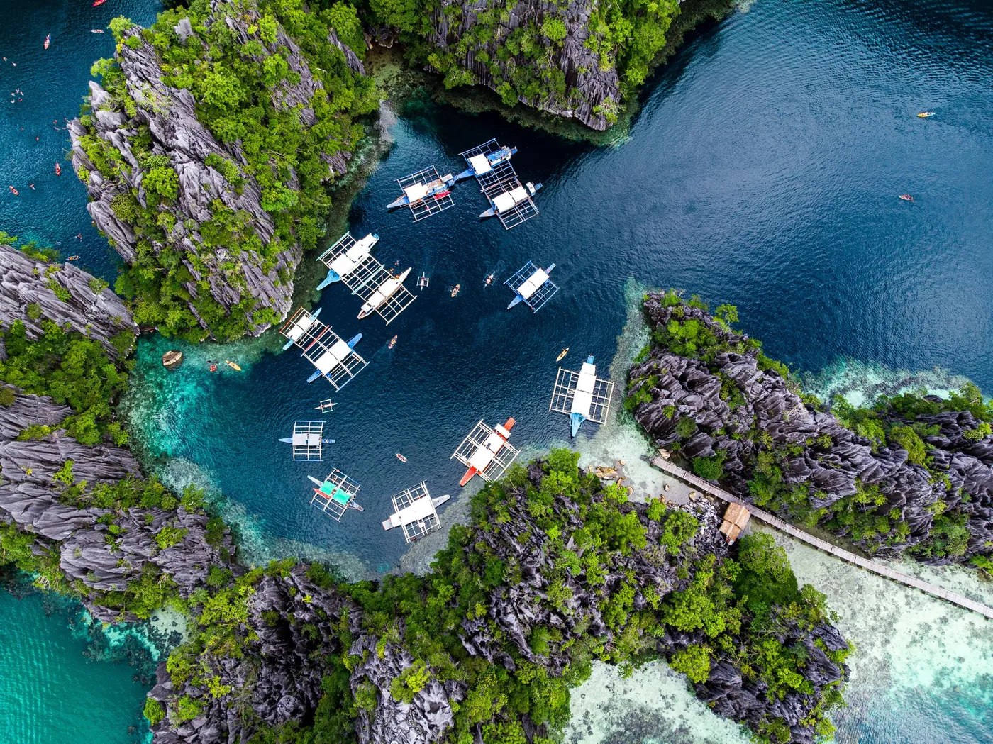 Aerial view of boats in a blue lagoon surrounded by limestone cliffs in El Nido, Palawan, Philippines